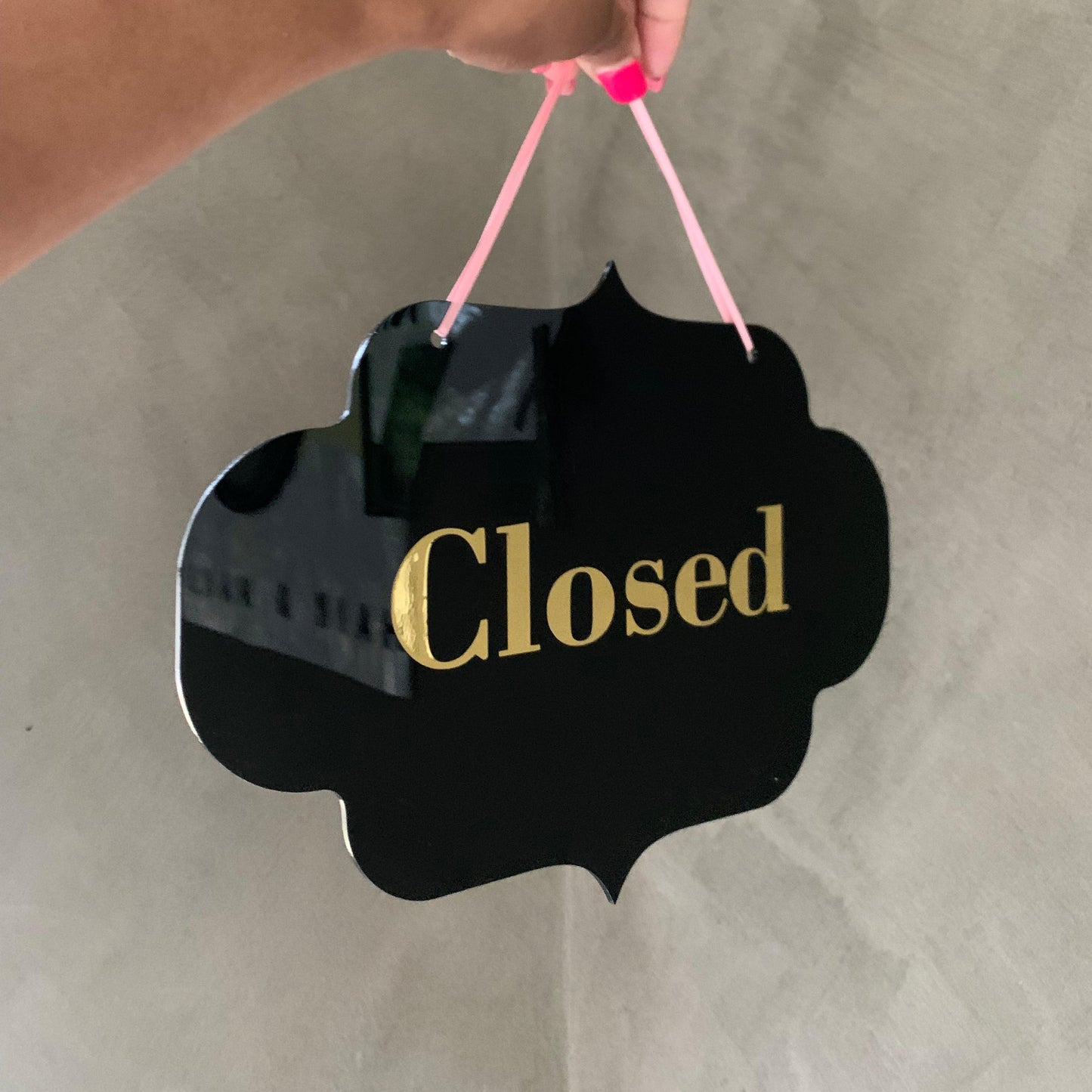Hand holding a 'Closed' sign with gold text on a plain background
