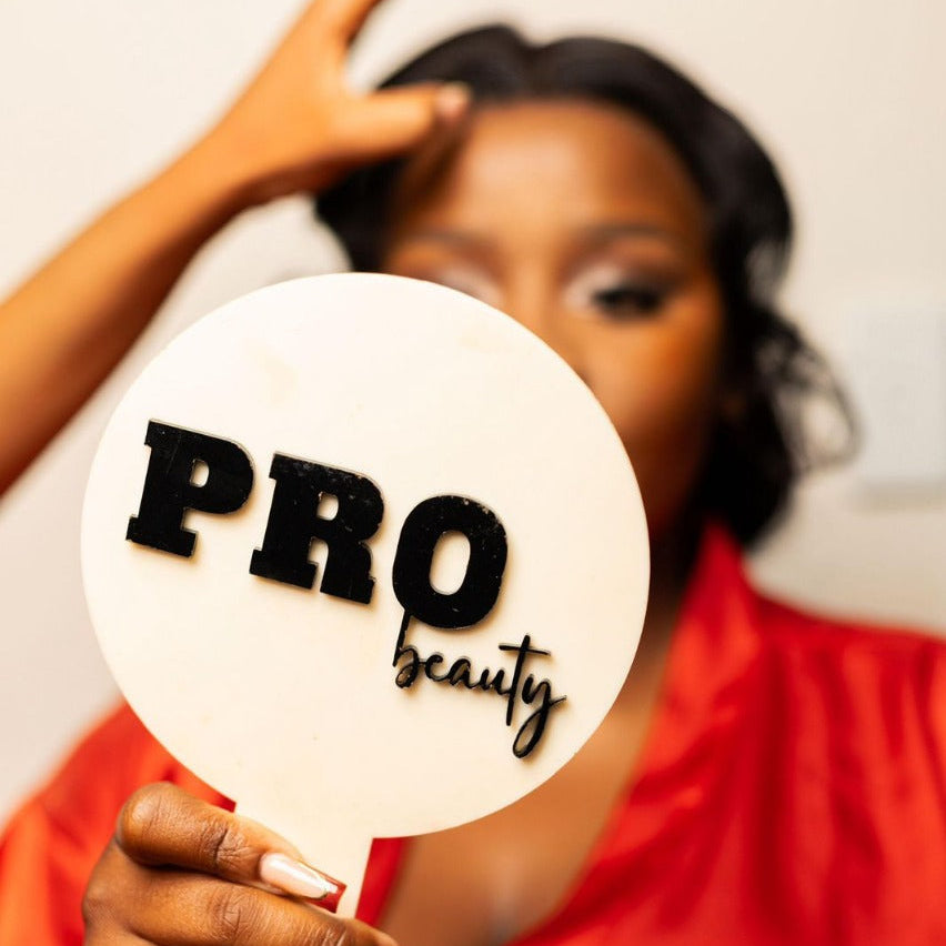 Woman holding a 'PRO beauty' acrylic hand mirror sign with a blurred background