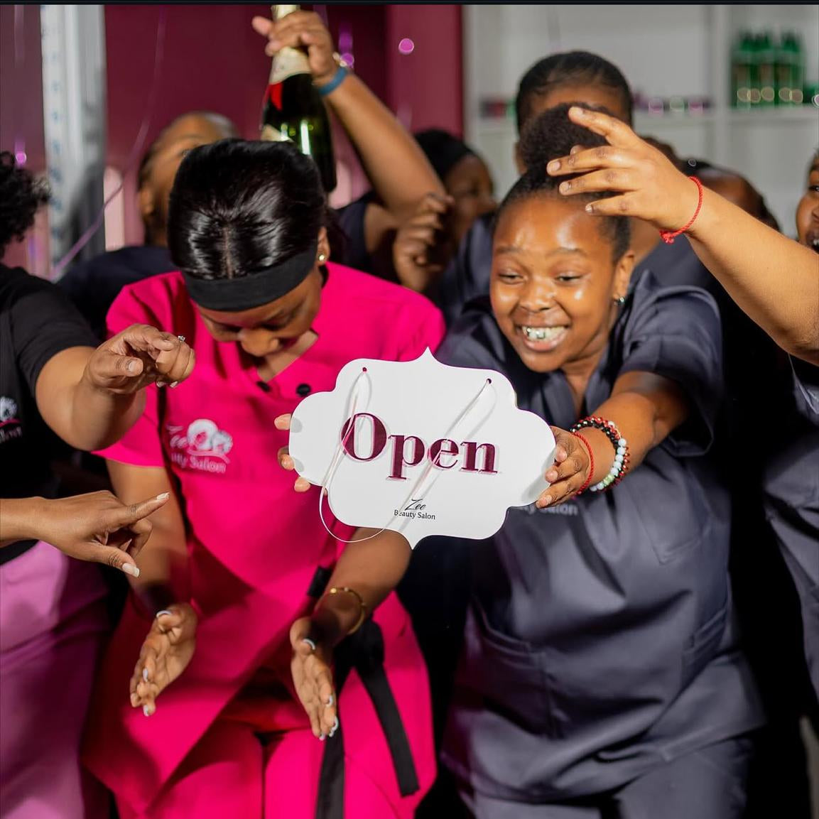 Two women holding a 'Open' sign with a celebratory atmosphere
