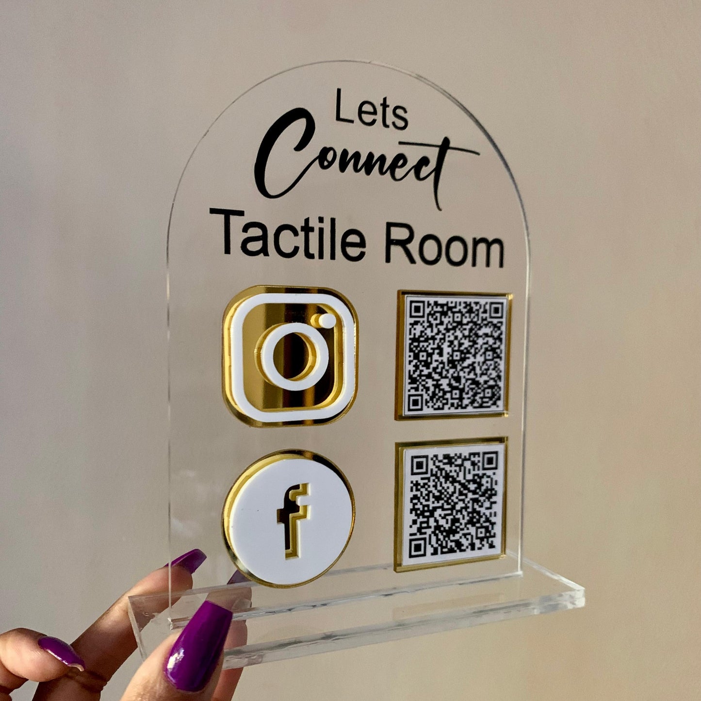 Clear acrylic sign with social media icons and QR codes held by a hand against a neutral background