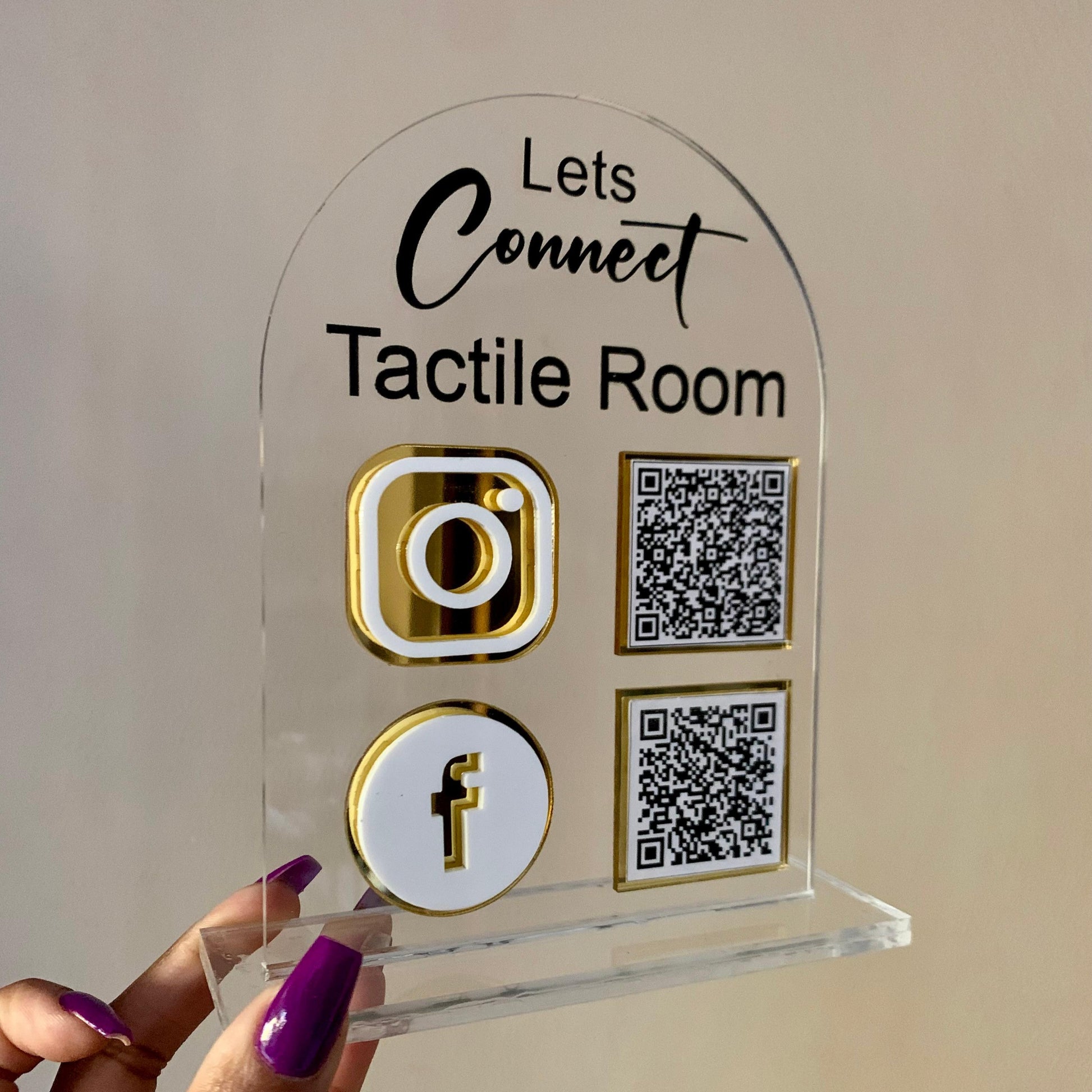 Clear acrylic sign with social media icons and QR codes held by a hand against a neutral background