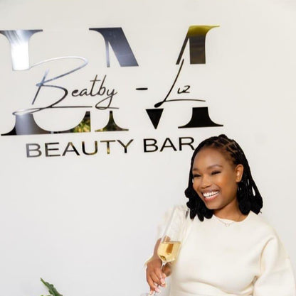 Woman in a white dress holding a glass of champagne in front of a 'LML Beauty Bar' sign.